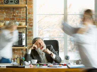 A nervous and exhausted boss works at his desk, surrounded by blurred, fast-moving employees—highlighting the stress, workplace anxiety, conflict, and burnout affecting the entire team