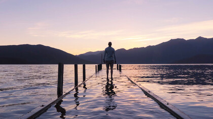 The tranquil scene of a person staring out over a body of water encapsulates the diverse philosophies on suffering, from Buddhism’s call for embracing both pleasure and pain, to Stoicism’s focus on control, and Islam’s emphasis on faith amid life's struggles