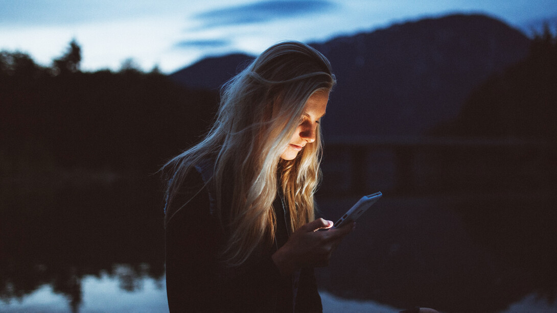 Mujer concentrada en su teléfono frente a un lago