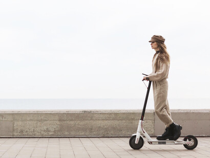 A young woman gliding on an electric scooter through a quiet, walkable city street, reflecting a calm and modern urban lifestyle