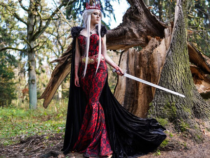 A woman in fantasy attire standing beside a tree in a mystical setting