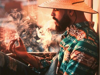 A man on a rooftop exhaling smoke from his rolled cigarette