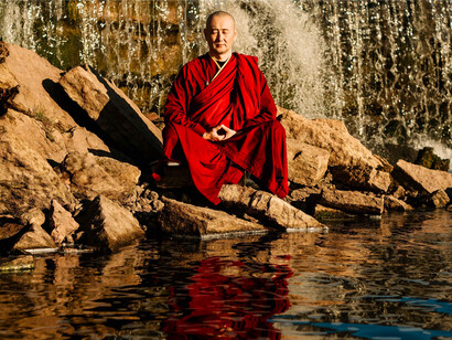 A monk meditating peacefully beside a waterfall, representing harmony between inner stillness and the rhythms of nature