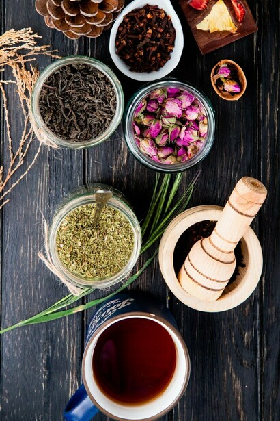 A bird's-eye view of an assortment of dried herbs and spices, including black tea leaves, peppermint, rose petals, and Ayurvedic herbs