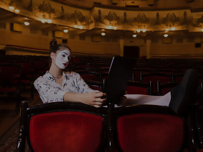 In the quiet of an auditorium, a lone female mime reads a manuscript, embodying the artistry and introspection of the performing arts