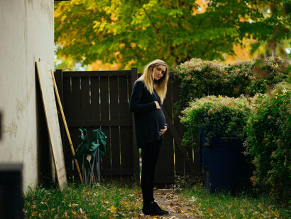 A teenage mother standing near a brown wooden fence, reflecting on her situation