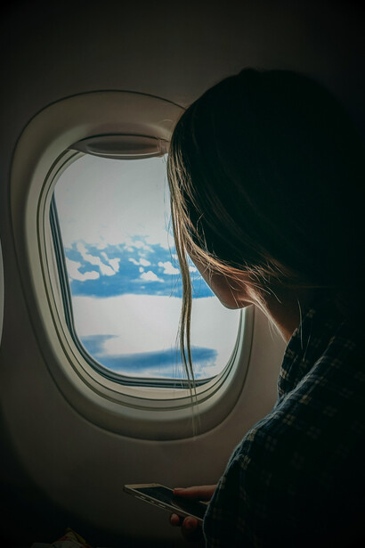 A hand reaches out to the sky through the airplane window, capturing a moment of wonder above the clouds