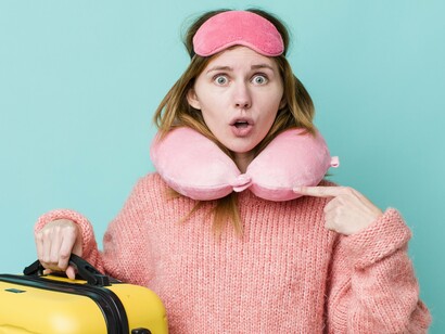 Wearing a pink neck pillow and holding a bright yellow suitcase, she exemplifies the article’s emphasis on comfort and preparation for stress-free travel