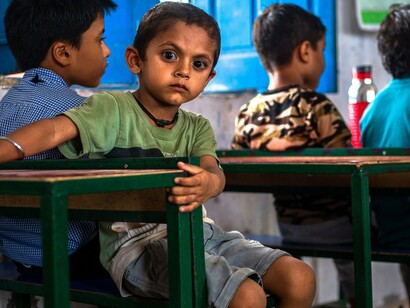 A child seated at a school desk while surrounded by classmates, symbolising the foundational role of education in shaping a better future