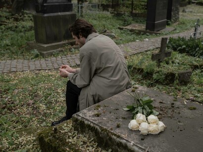 A man sitting grieving over his lost loved one as after placing white roses on their tomb