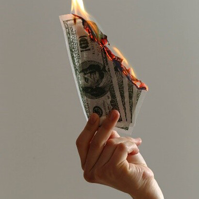 Amidst the economic crisis, a person holds lighted dollar bills, depicting the burning effects of financial instability and the struggle to keep money from slipping away