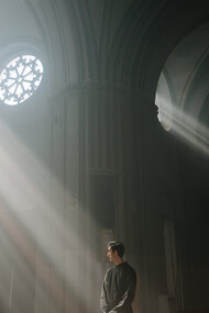 The rays cutting through the darkness serve as a poignant metaphor for the search for truth in a world where faith can be both a refuge and a tool for power 