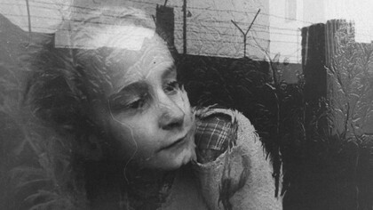 Una niña mira pensativa a través del cristal de la ventana de su apartamento, que refleja la imagen de la cerca de alambre de púas que corona el Muro de Berlín, en diciembre de 1962