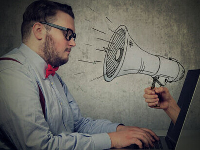 A man sitting at a desk, working on his computer, screams as a megaphone emerges from the laptop screen