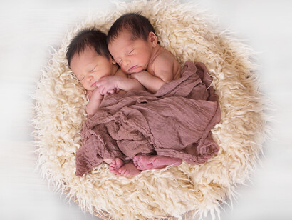 Two twin babies snuggled together on a pillow sleeping