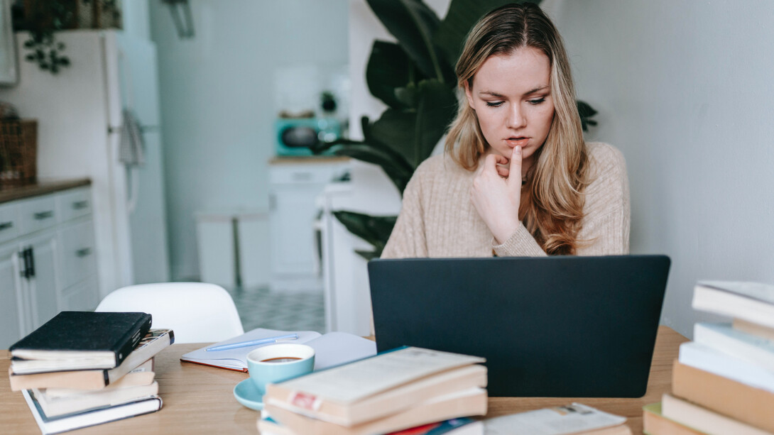 Escritora lê livros físicos e escreve suas anotações no computador