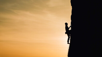 Scaling life's peaks metaphorically, the arduous climb reflects the challenges of achieving success and wealth, mirroring the uphill struggle toward prosperity