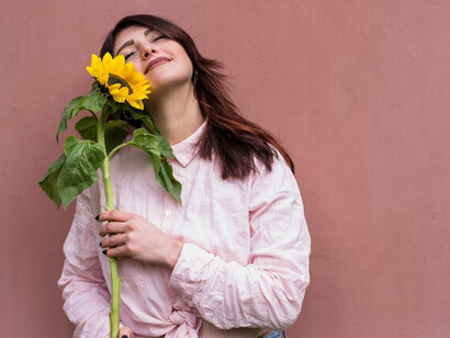 A woman holding a fresh yellow flower near her face, embodying self-love, authenticity, personal growth, and embracing her uniqueness and the freedom to fail
