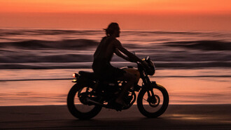 Homem pilota moto em areia da praia próximo ao mar