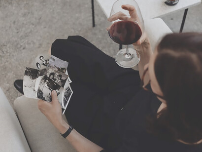 With a wine glass in hand, the woman gazes upon the photos, her eyes reflecting a mixture of sadness and longing