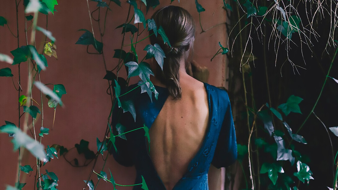 A woman in a blue dress, viewed from behind, standing near an old building