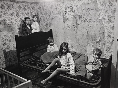 Mr and Mrs M and their four children lived in a council owned house in Vincent Crescent, Balsall Heath. Apart from the poor state of the property – no bathroom, no hot water, outside lavatory, inside walls running with damp – these children were sleeping in the middle of winter, on two sodden seat cushions covered by a couple of old ‘macs’, there was no heating in the room, the snow lay thick outside and the windows were broken. Birmingham, January 1969 © Nick Hedges / National Media Museum, Bradford
