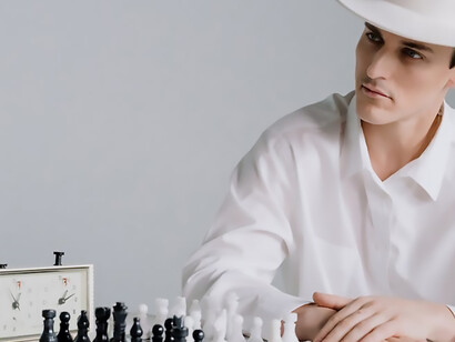 Seated before a chessboard, a man elegantly attired in a white shirt and a complementing white hat exudes an air of concentration, ready to engage in a strategic chess duel
