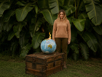 In a silent tropical landscape, a burning globe rests above a woman’s outstretched hands, capturing the tension between environmental beauty and planetary destruction
