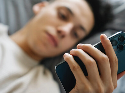 Ragazzo sul proprio letto con gli occhi fissi sul cellulare 