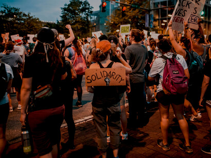 Anonymous demonstrators march in an anti-racism solidarity protest, holding banners in support of freedom, democracy, and social justice