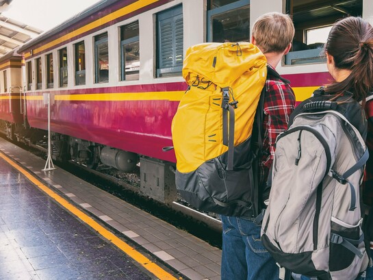Um homem e uma mulher esperam pelo trem em uma estação, prontos para seguir viagem. Sair do lugar que conhecemos é também um exercício de humildade diante de outras paisagens, culturas e formas de viver