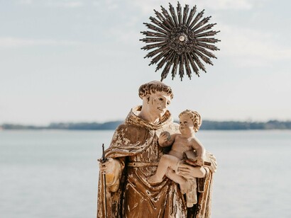 A imagem mostra uma representação de Santo Antônio diante do mar, com o Menino Jesus nos braços e uma auréola em destaque. A figura do santo, tradicionalmente associada à devoção popular e aos pedidos por casamento, ocupa papel central na narrativa de Socorro Acioli
