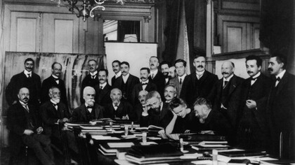 Participantes del I Congreso Solvay (1911) sobre «la radiación y los cuantos». Curie (sentada, segunda a la derecha y con la cabeza apoyada sobre su mano) conversa con Henri Poincaré; detrás de ellos, un joven Albert Einstein