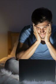 Late at night, a man stares at his computer screen, insomnia keeping him awake
