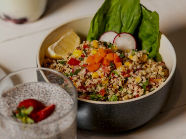 Sliced fruits, quinoa, and fresh vegetables served in a black ceramic bowl as a wholesome low-calorie meal