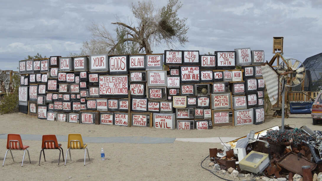Ell muro de la verdad en Slab City; televisores con palabras de noticias falsas y mensajes de propaganda frente a deshechos electrónicos