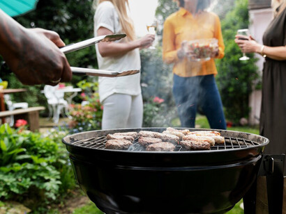 A man preparing a barbecue for a family gathering, with food sizzling on the charcoal grill and flames rising from the coals