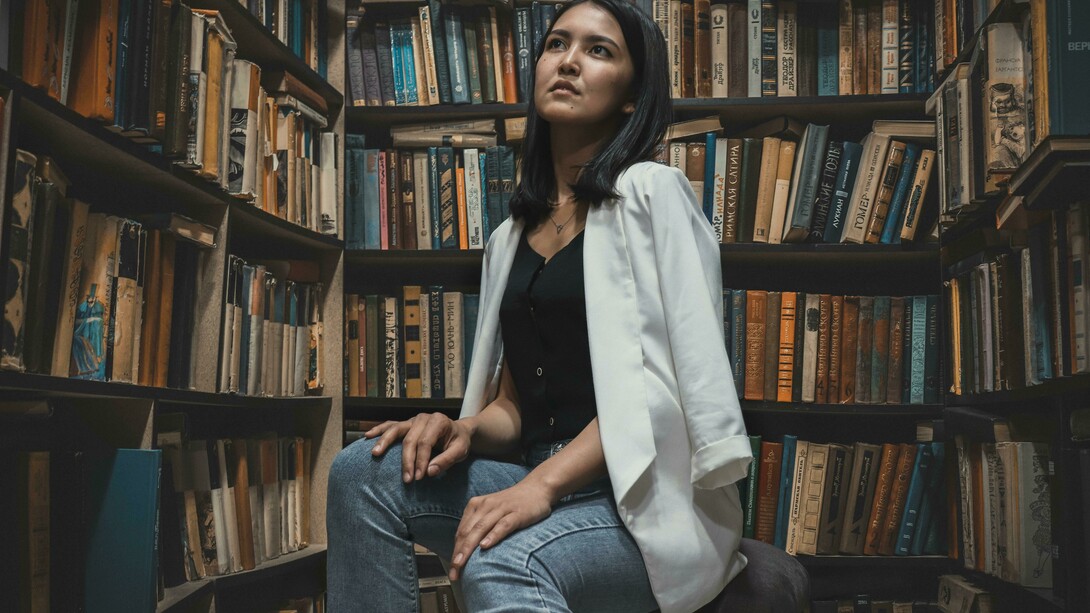 A woman sits in an academic library in Asia, surrounded by shelves filled with books