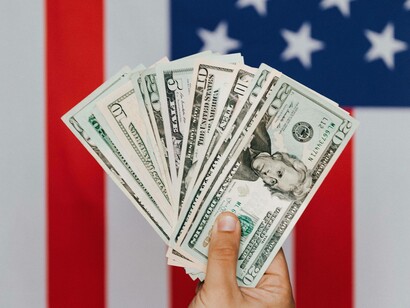 Person hält amerikanische Banknoten vor einer US-Flagge hoch