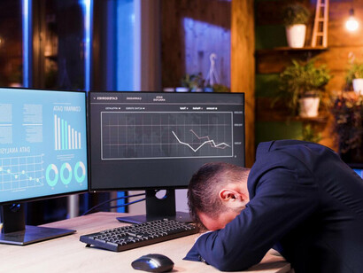 The manager put his head on his desk, while reviewing financial graphs and stock market data on the monitor, focusing on options trading