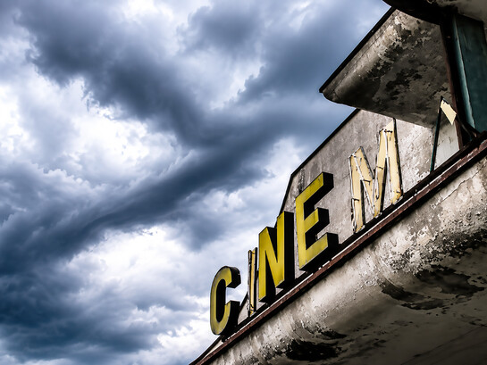 Abandoned movie theater standing silent beneath a stormy sky, evoking nostalgia, decay, and the fading echoes of a once-vibrant past