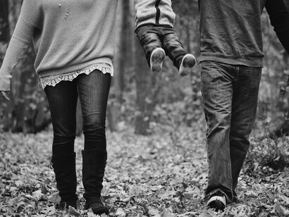 A couple play swing with their child while walking on an autumn forest