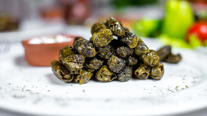 Yaprak sarması features minced meat and spices wrapped in grape leaves, served with plain yogurt, showcasing a classic side of Turkish cuisine