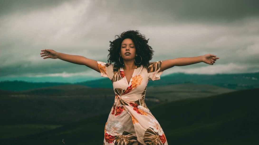 A woman in a white and red floral dress standing on a green grass field, representing freedom, self-acceptance, and openness