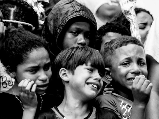 Crianças durante o velório e enterro de seu amigo, Thiago Menezes Flausino, de 13 anos, morto pela polícia. O registro foi feito pela fotógrafa Selma Souza em 2023, no Rio de Janeiro, Brasil. A pessoa deixa de ser João, Mariah, Benhur e passa a ser o maconheiro, o ladrão. Esse caso escancara a aceitação da violência policial contra adolescentes pobres e a necropolítica que decide que a vida de Benhur não importa
