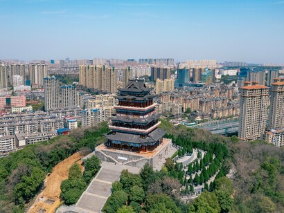 O monumento histórico domina a paisagem enquanto a cidade se expande ao fundo. O contraste visual reforça a ideia de ciclos de desenvolvimento abordada pelo autor