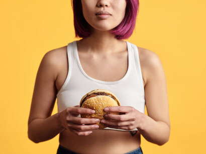 Donna in canotta bianca con un hamburger in mano 