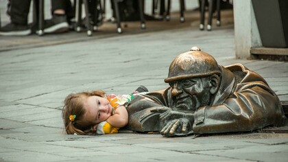A little girl lies on the street beside a statue in Bratislava, Slovakia