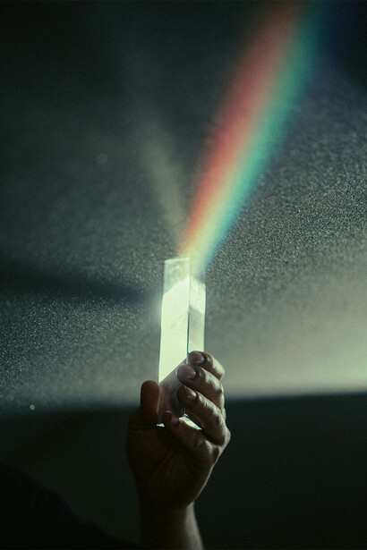 Mão segurando cristal que recebe luz e a divide em espectros coloridos. 
Cada composição química e atômica dos cristais emana um tipo característico de energia através do seu campo