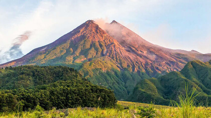 The serene beauty of Mount Merapi in Indonesia stands in stark contrast to its powerful history, with lush greenery enveloping its slopes and the clear blue skies above